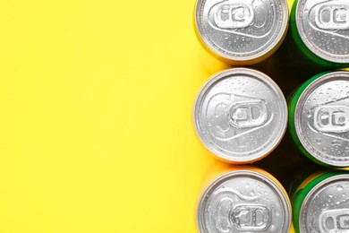 Photo of Energy drinks in wet cans on yellow background, top view. Space for text