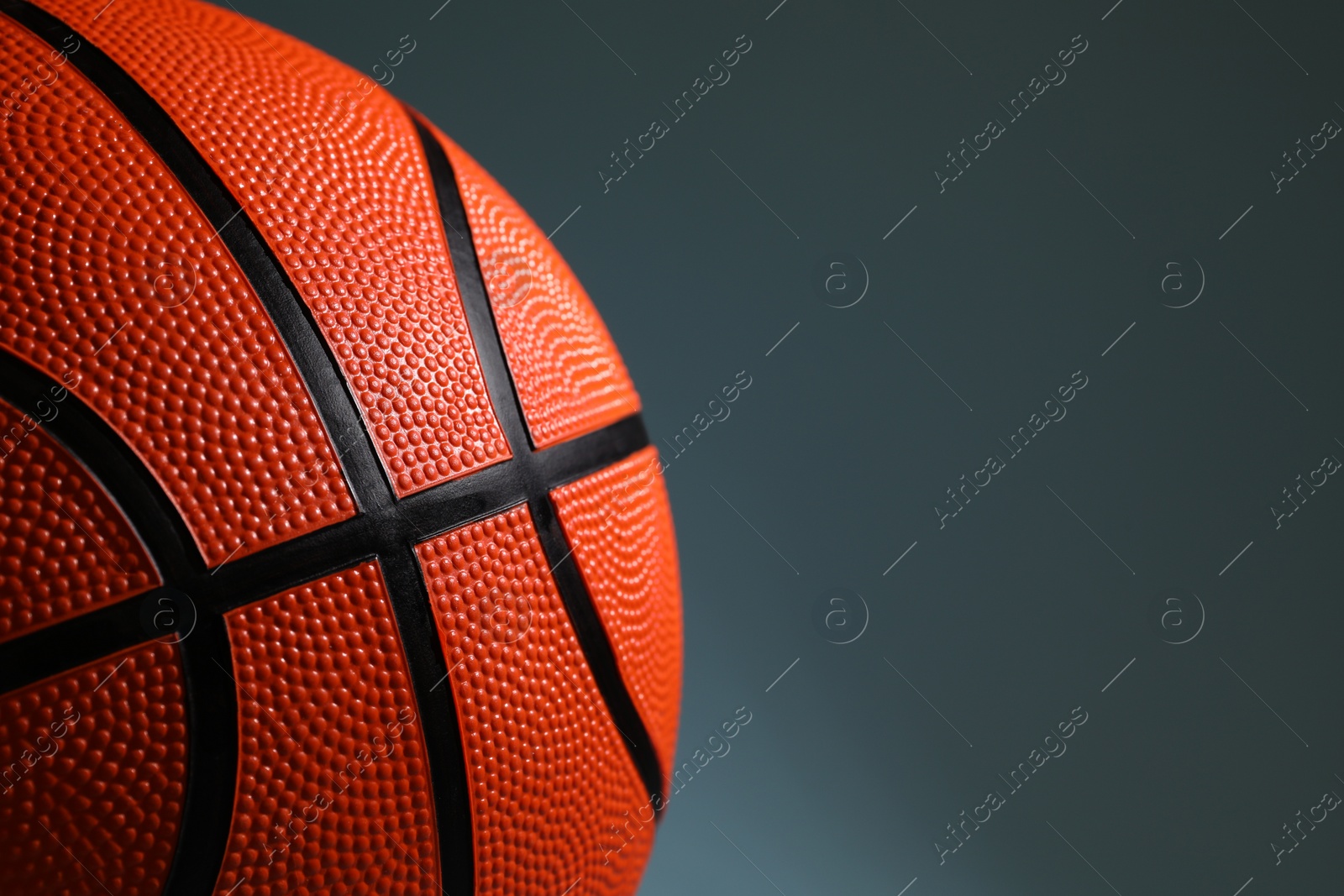 Photo of One orange basketball ball on dark grey background, closeup. Space for text