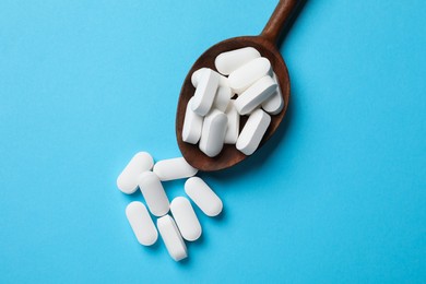 Vitamin capsules in wooden spoon on light blue background, top view