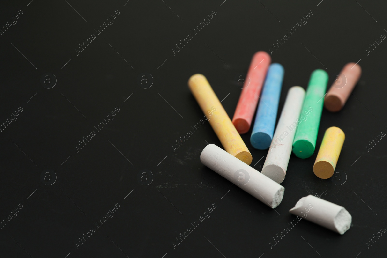 Photo of Colorful chalks on black board, closeup. Space for text