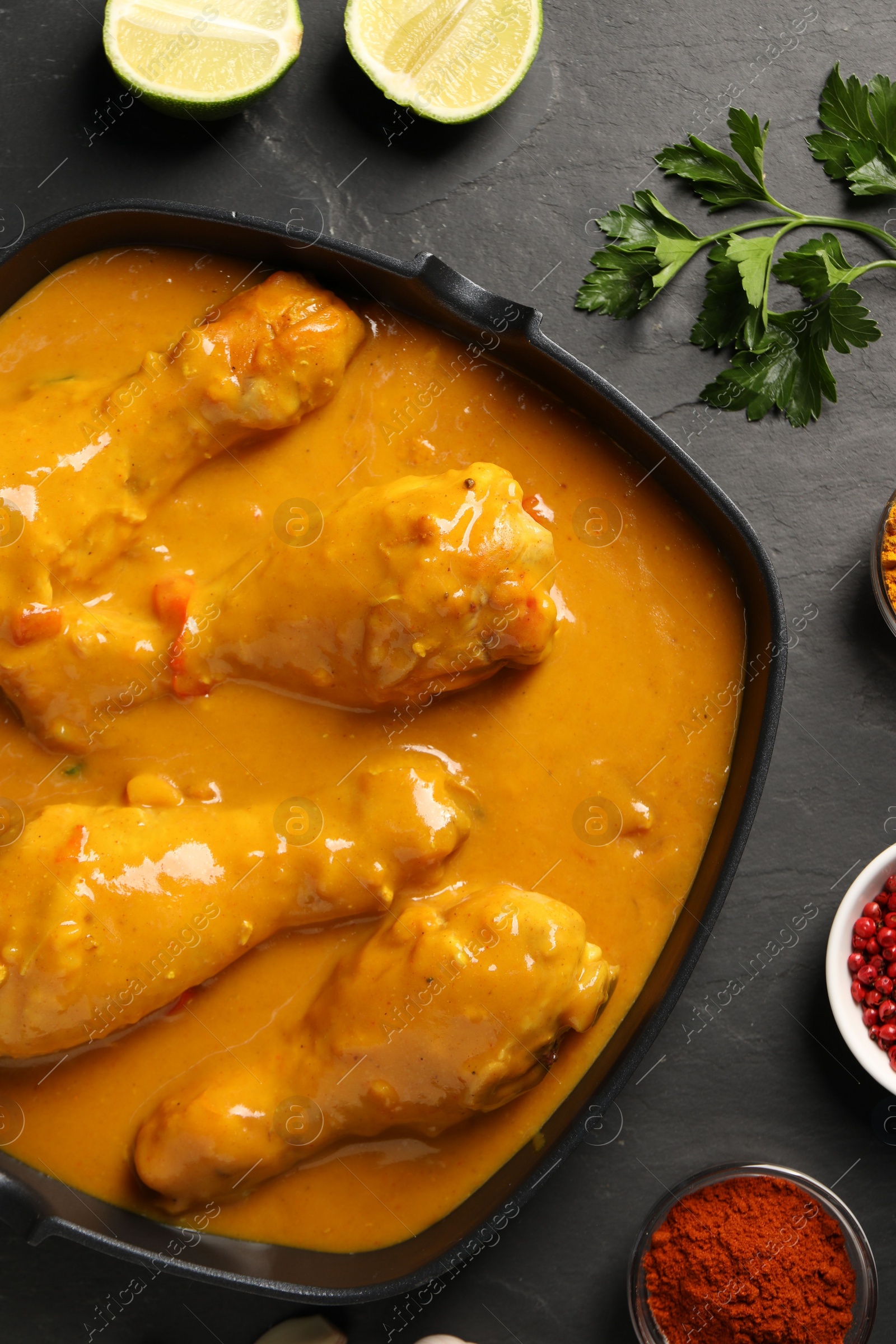 Photo of Tasty chicken curry and ingredients on black textured table, flat lay