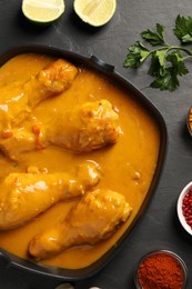 Tasty chicken curry and ingredients on black textured table, flat lay