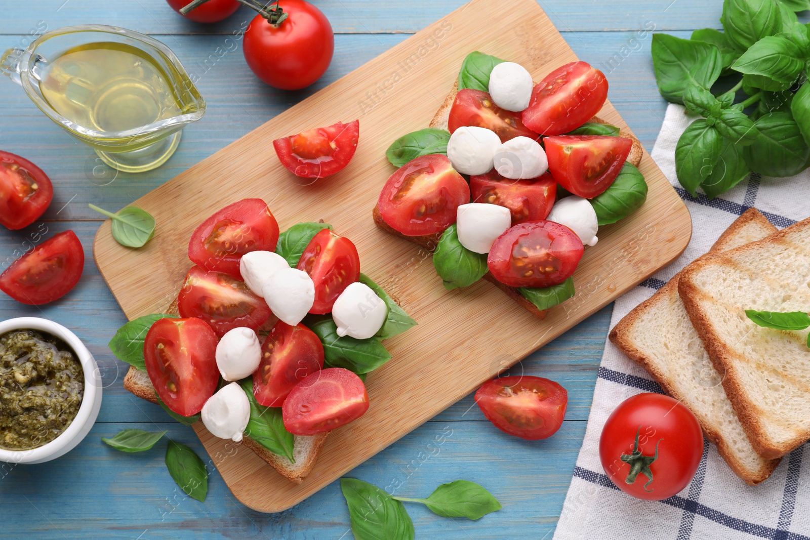 Photo of Delicious Caprese sandwiches with mozzarella, tomatoes, basil and pesto sauce on light blue wooden table, flat lay