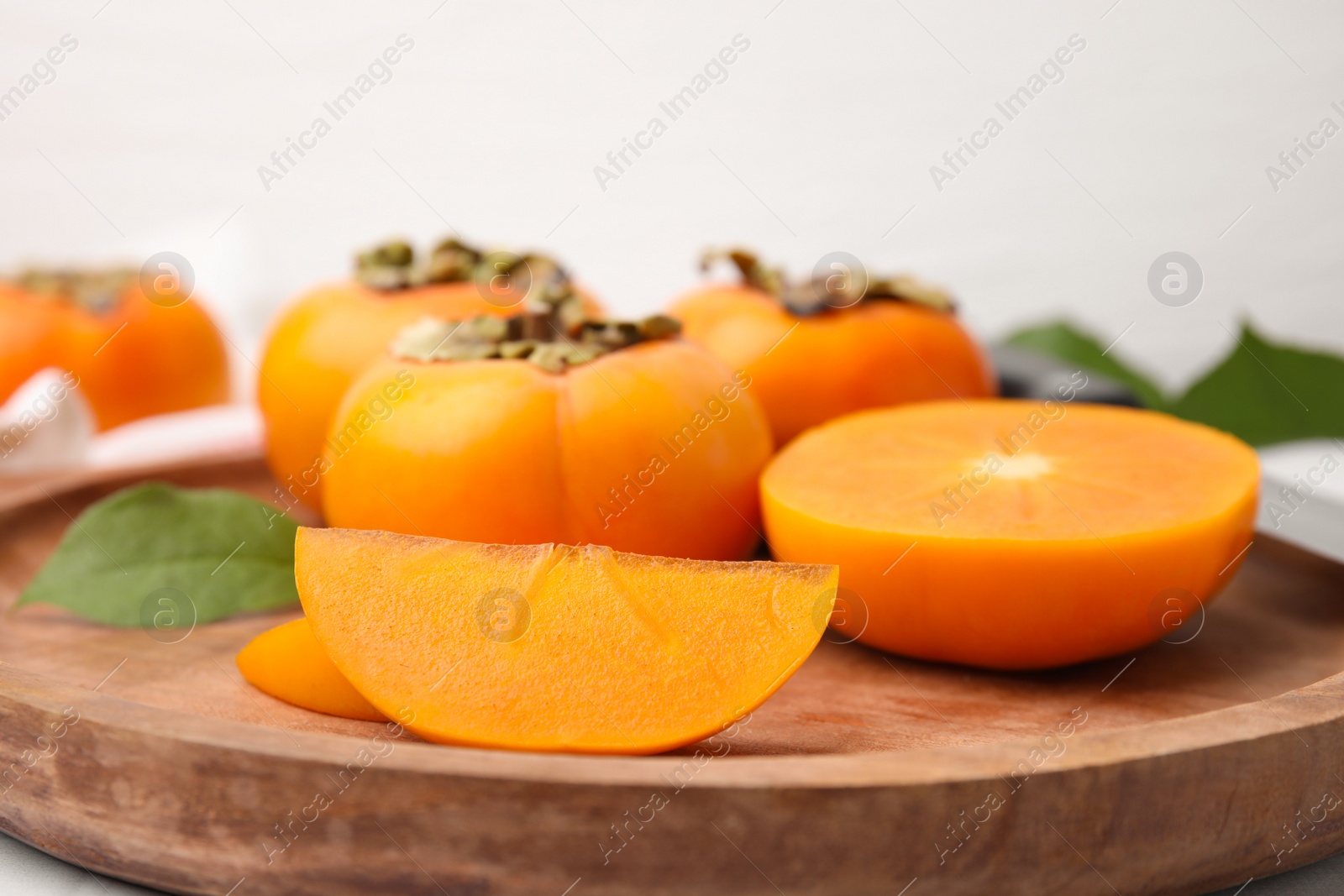 Photo of Wooden tray with whole and cut delicious ripe persimmons, closeup