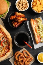 Photo of Chicken wings, onion rings and other fast food on black wooden table, flat lay