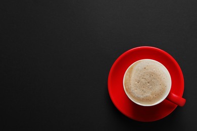 Photo of Red cup with aromatic cappuccino on black background, top view. Space for text