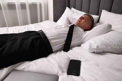 Photo of Businessman in office clothes resting on bed indoors