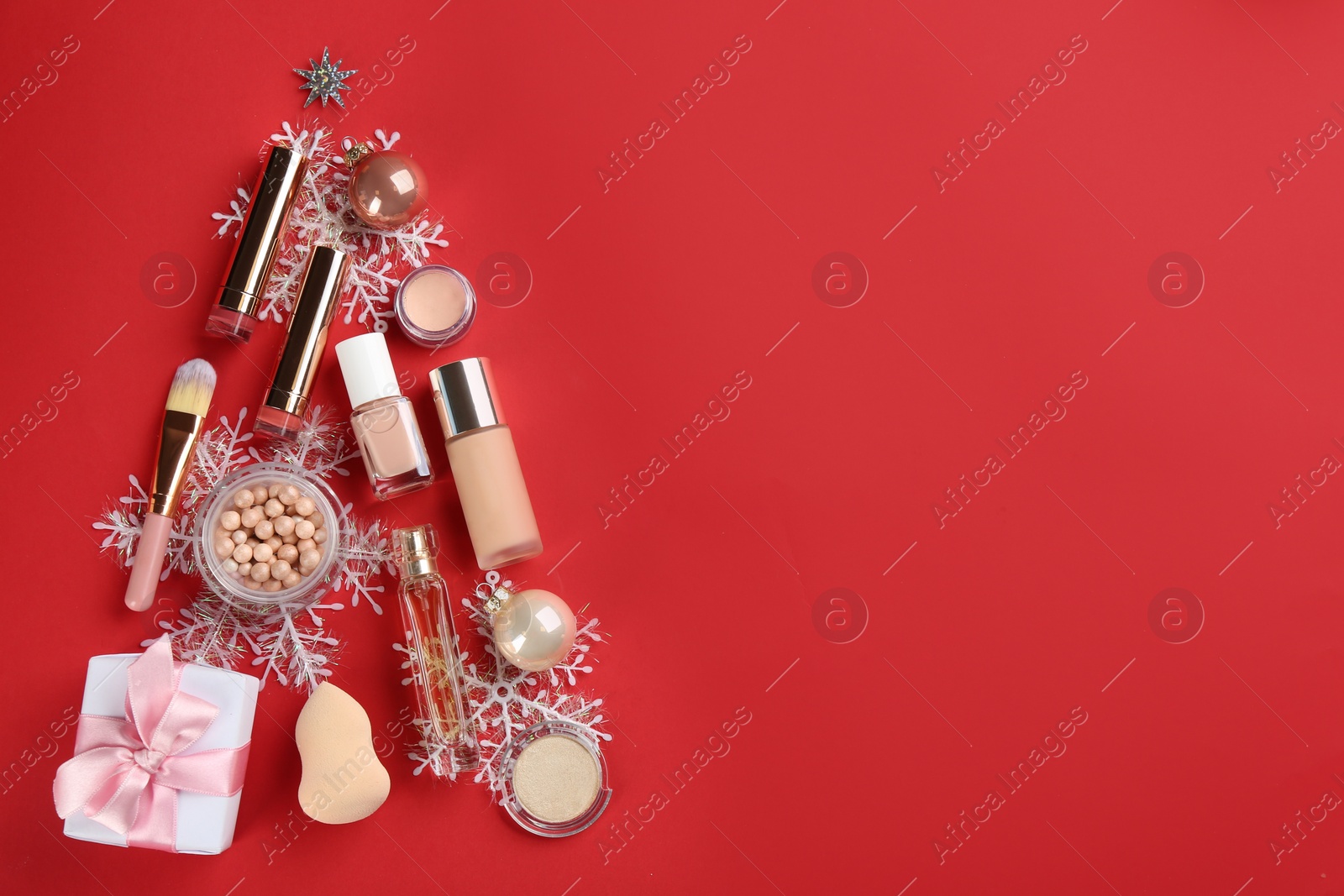 Photo of Christmas tree shape of decorative cosmetic products on red background, flat lay with space for text. Winter care