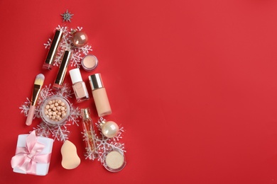 Photo of Christmas tree shape of decorative cosmetic products on red background, flat lay with space for text. Winter care