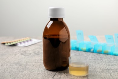 Photo of Bottle of syrup and measuring cup on light grey table. Cold medicine