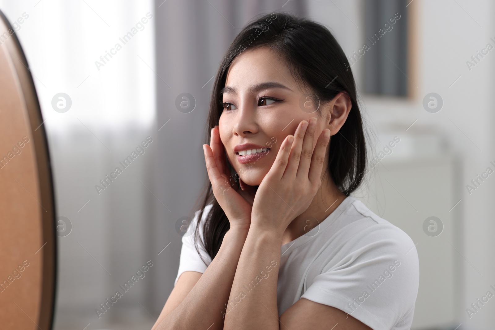 Photo of Woman with perfect skin looking at mirror indoors