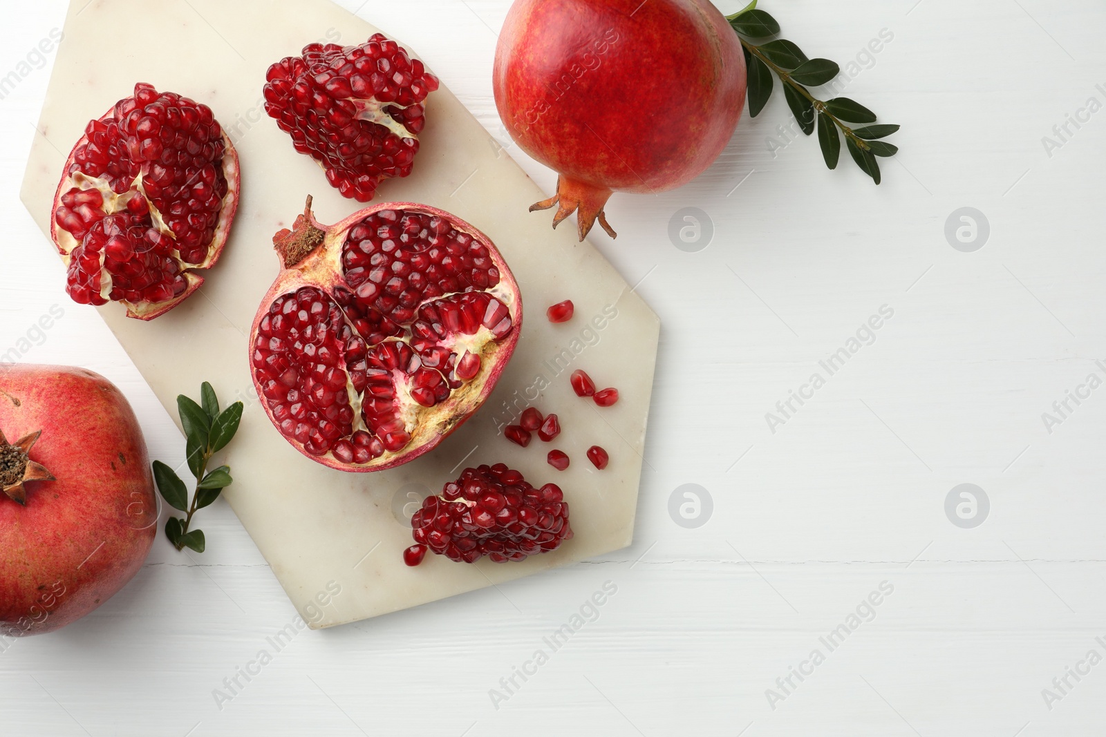 Photo of Fresh pomegranates and branches on white wooden table, flat lay. Space for text