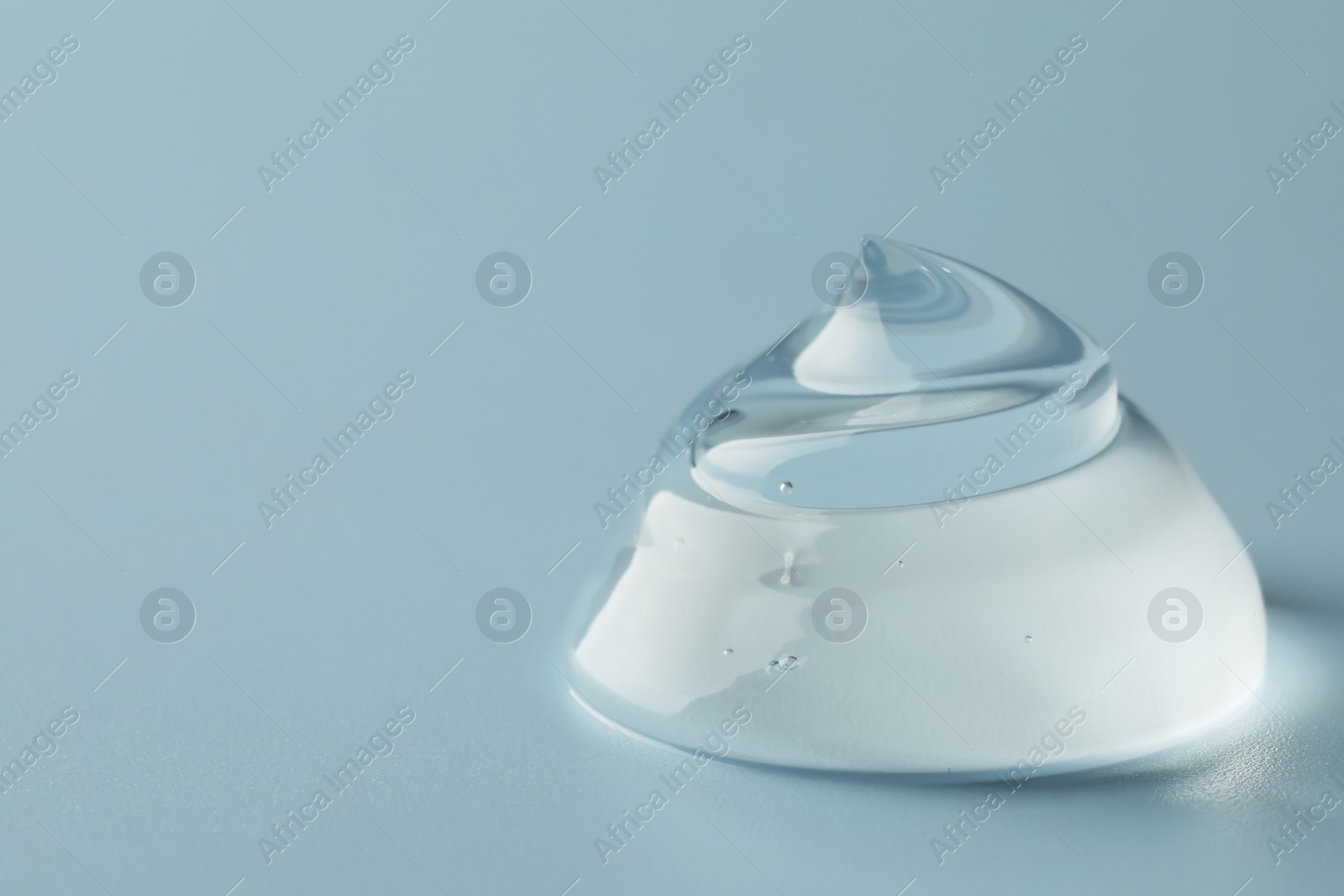 Photo of Sample of clear cosmetic gel on light blue background, closeup. Space for text