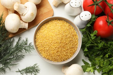 Photo of Raw bulgur in bowl, vegetables and herbs on white table, flat lay