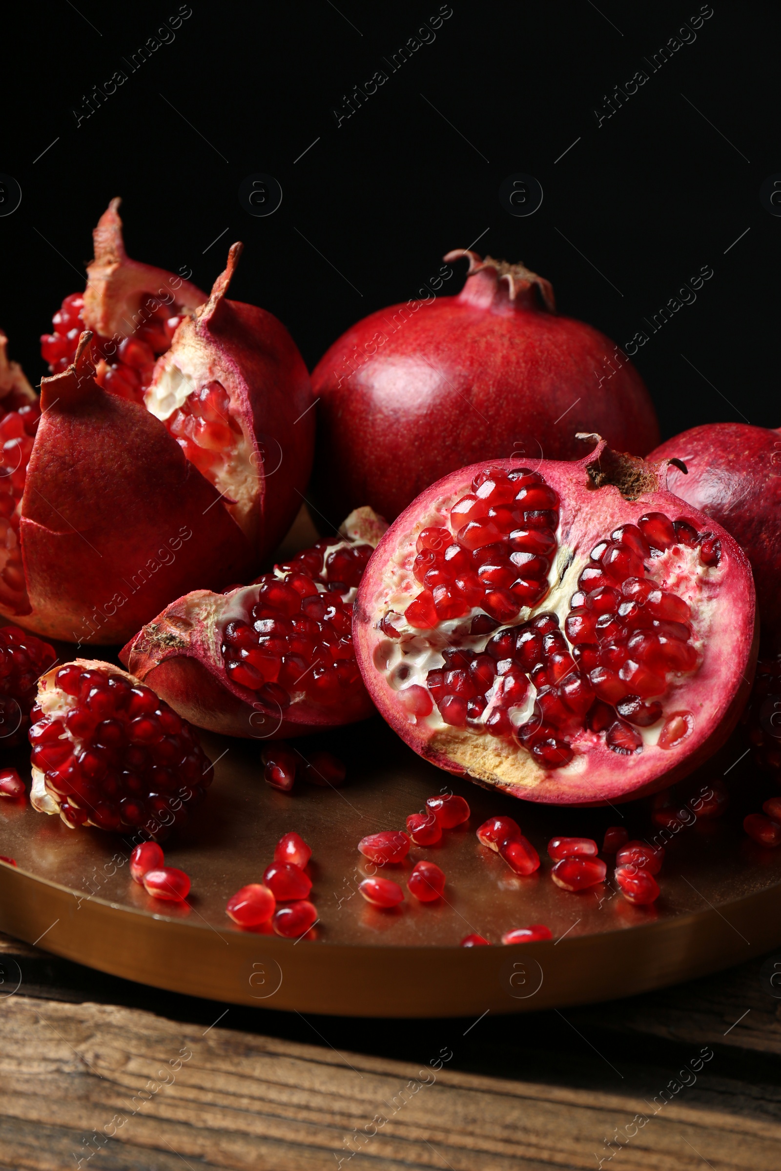 Photo of Tray with ripe pomegranates on table against black background