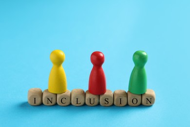 Photo of Colorful pawns and wooden cubes with word Inclusion on light blue background, closeup