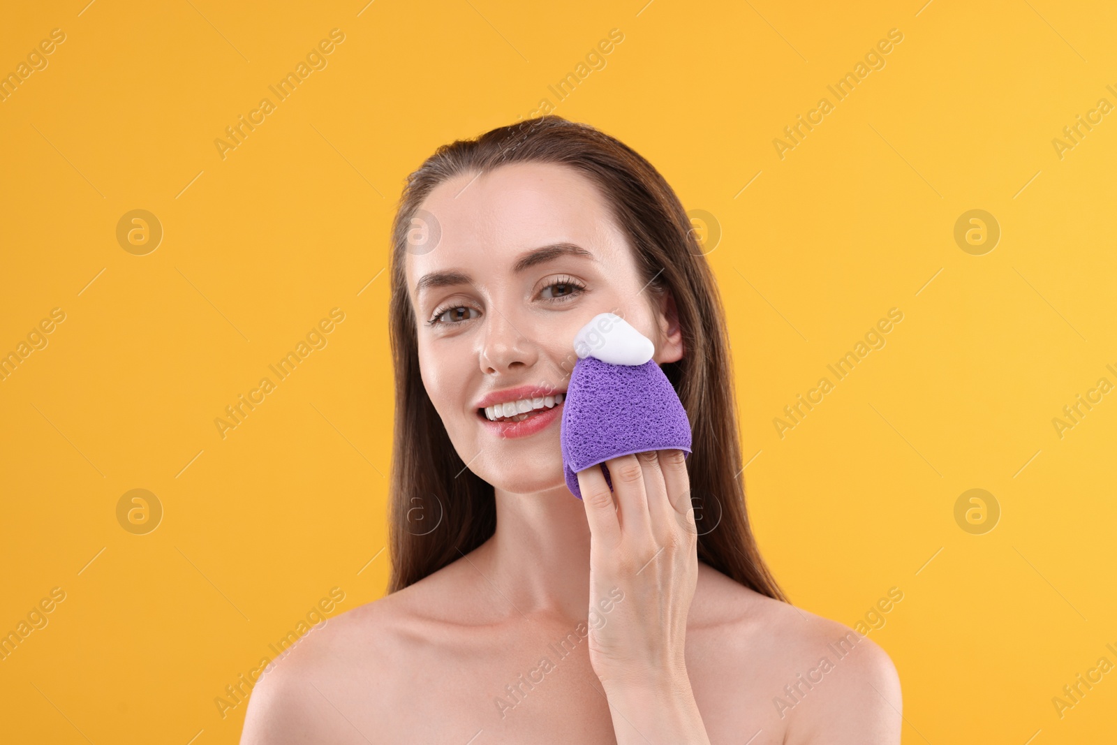 Photo of Happy young woman washing her face with sponge on orange background
