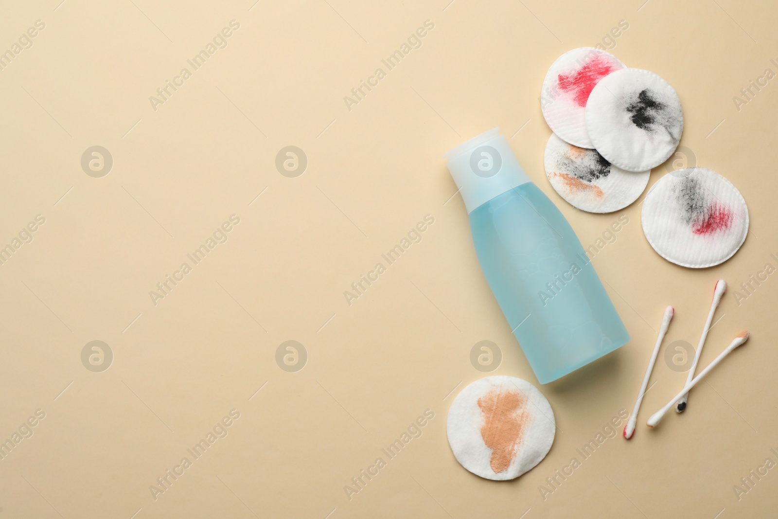 Photo of Dirty cotton pads, swabs and makeup removal product on beige background, flat lay. Space for text