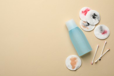 Photo of Dirty cotton pads, swabs and makeup removal product on beige background, flat lay. Space for text