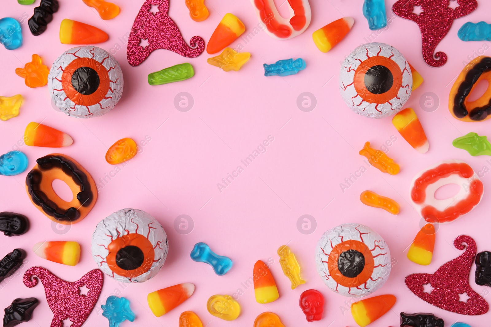 Photo of Frame made of tasty candies and Halloween decorations on pink background, flat lay. Space for text