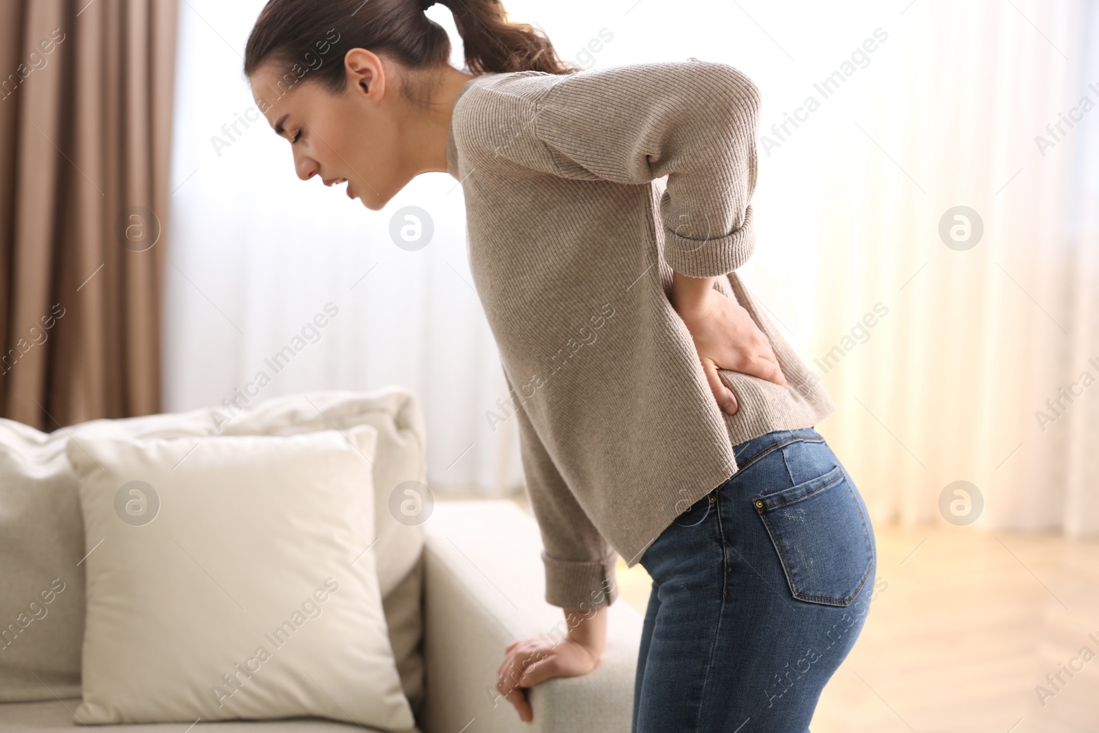 Photo of Woman suffering from back pain at home. Bad posture problem