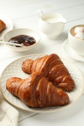 Photo of Plate with tasty croissants served on white wooden table, closeup