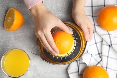 Woman squeezing orange juice at grey table, top view