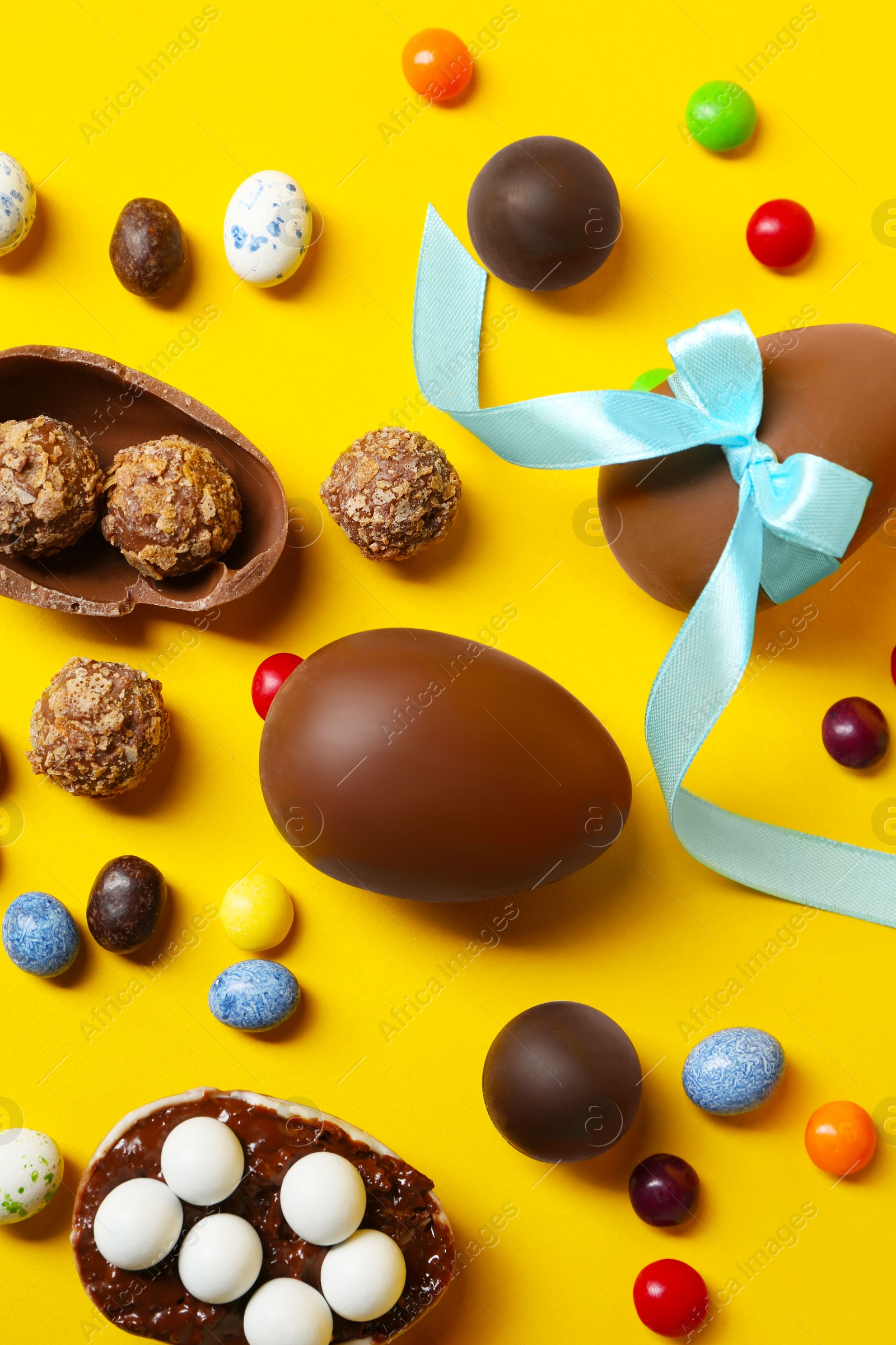 Photo of Tasty chocolate eggs and candies on yellow background, flat lay