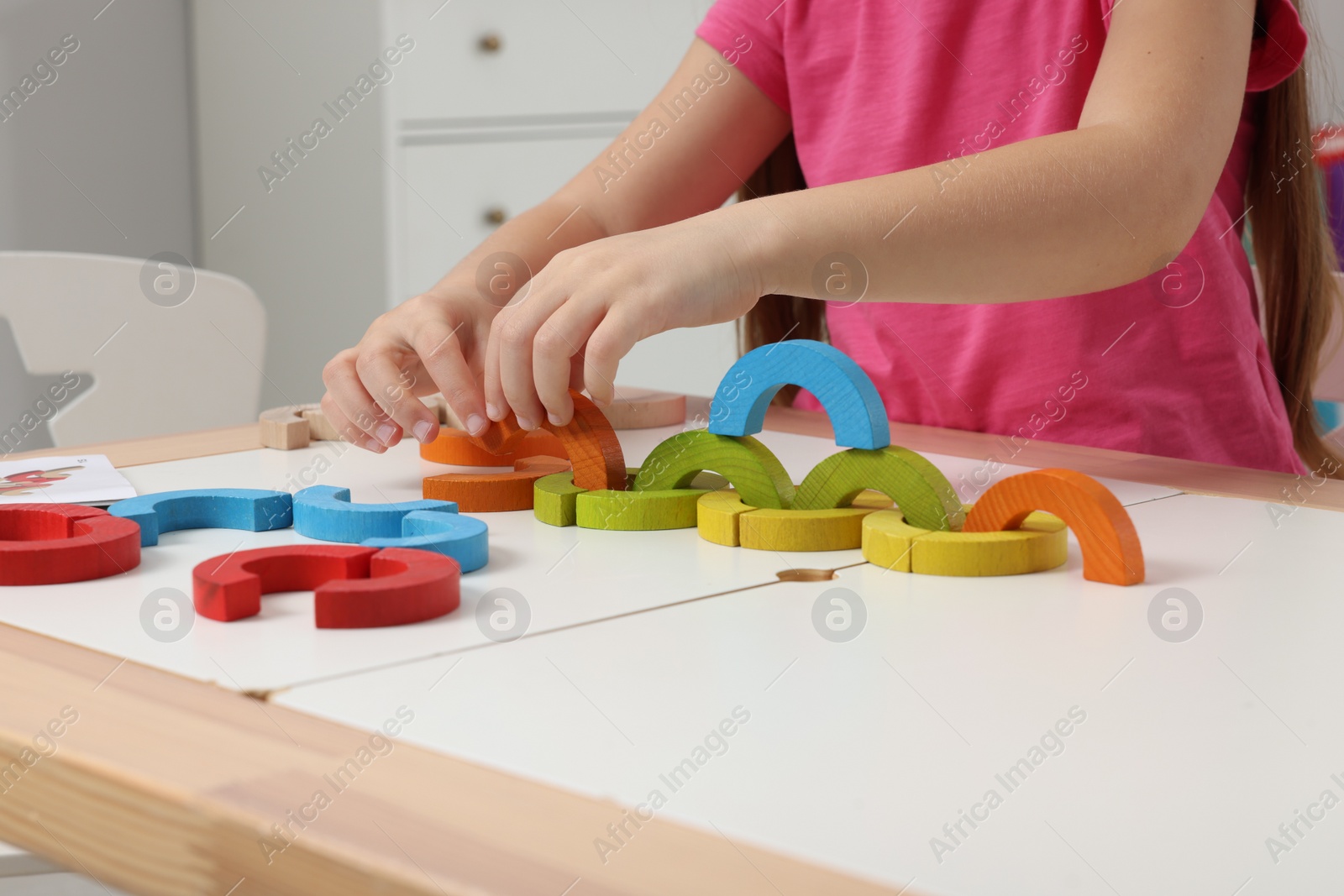 Photo of Motor skills development. Girl playing with colorful wooden arcs at white table indoors, closeup