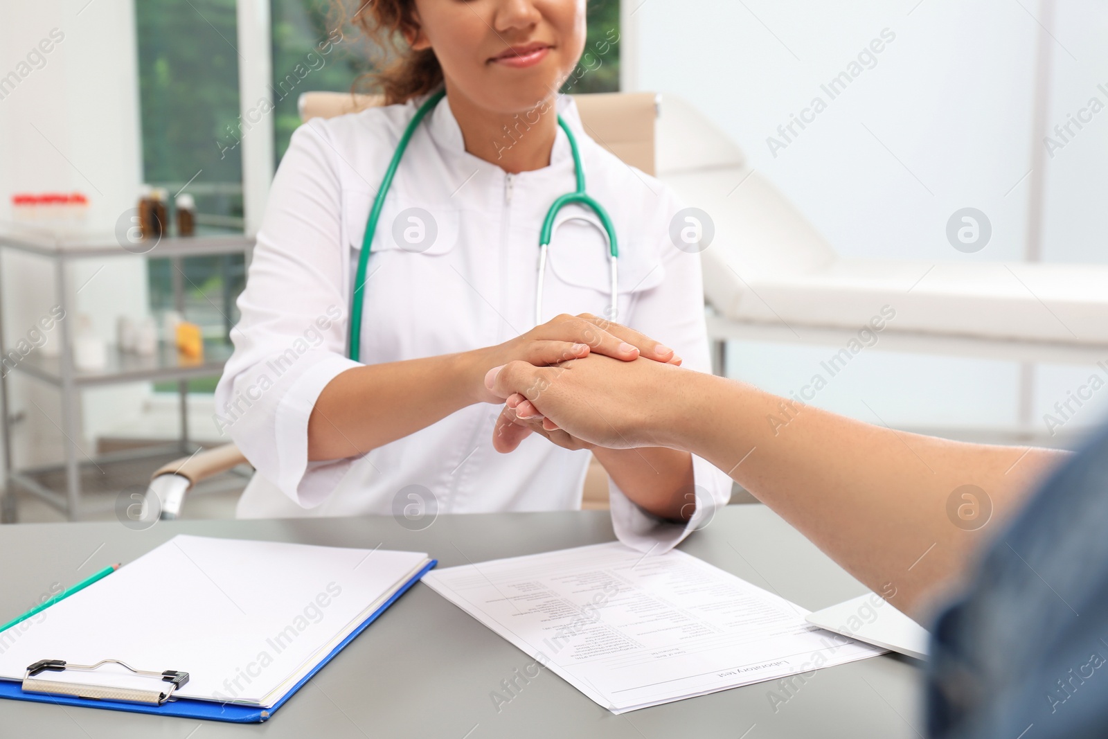 Photo of African American doctor comforting patient at table in hospital, closeup