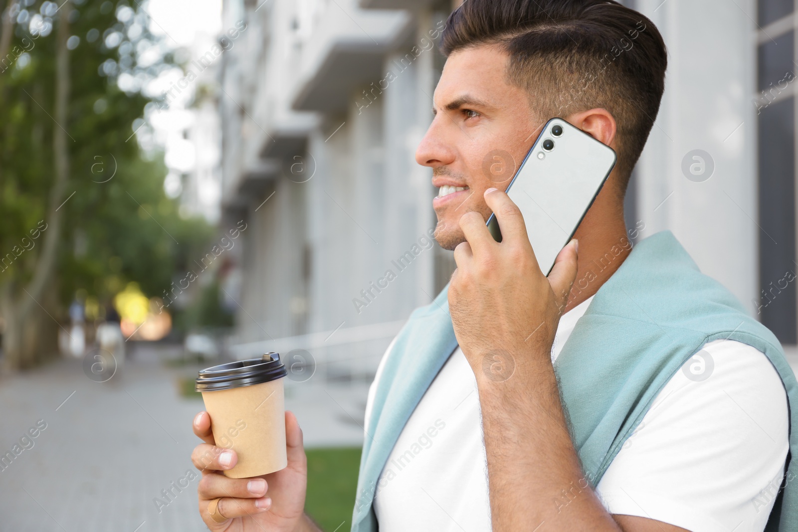 Photo of Man with cup of coffee talking on modern mobile phone outdoors