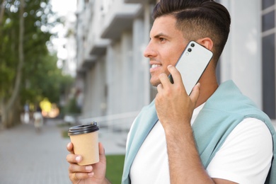 Photo of Man with cup of coffee talking on modern mobile phone outdoors