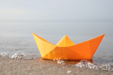 Photo of Orange paper boat on sandy beach near sea, closeup