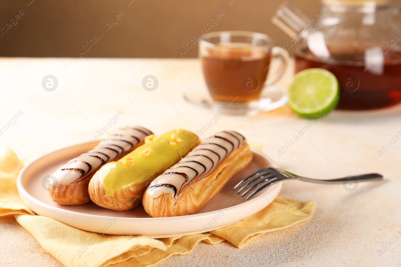 Photo of Different tasty glazed eclairs served on color textured table, closeup