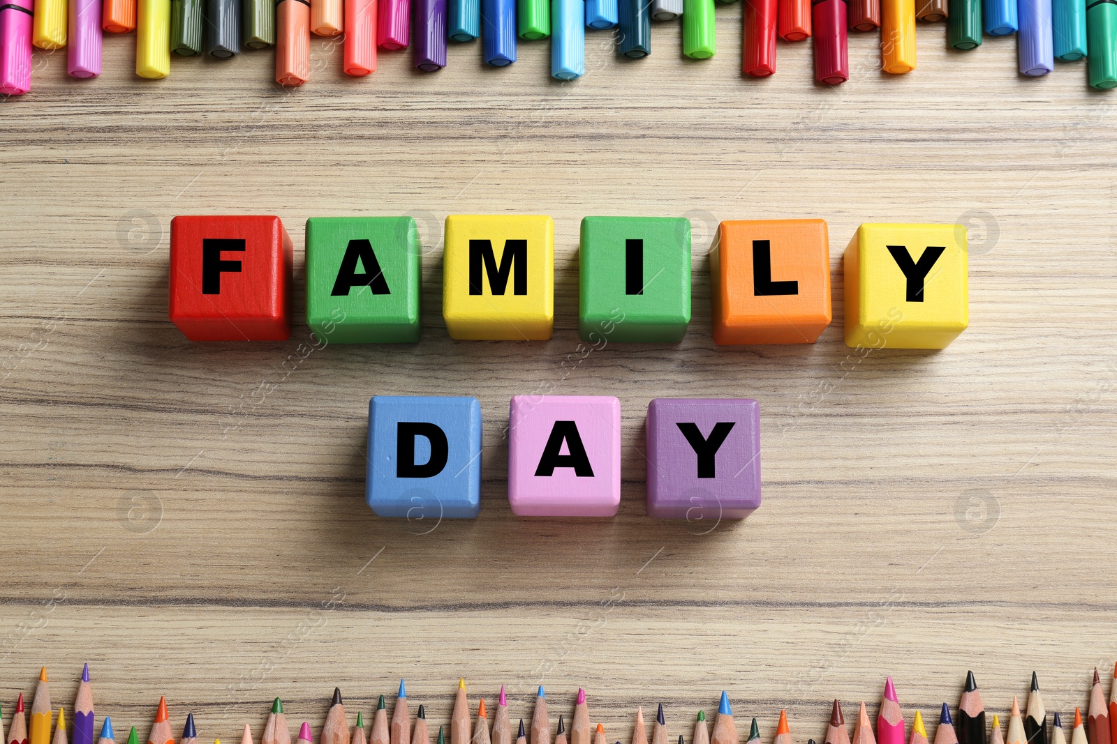 Photo of Colorful cubes with words Family Day, pencils and felt tip pens on wooden background, flat lay