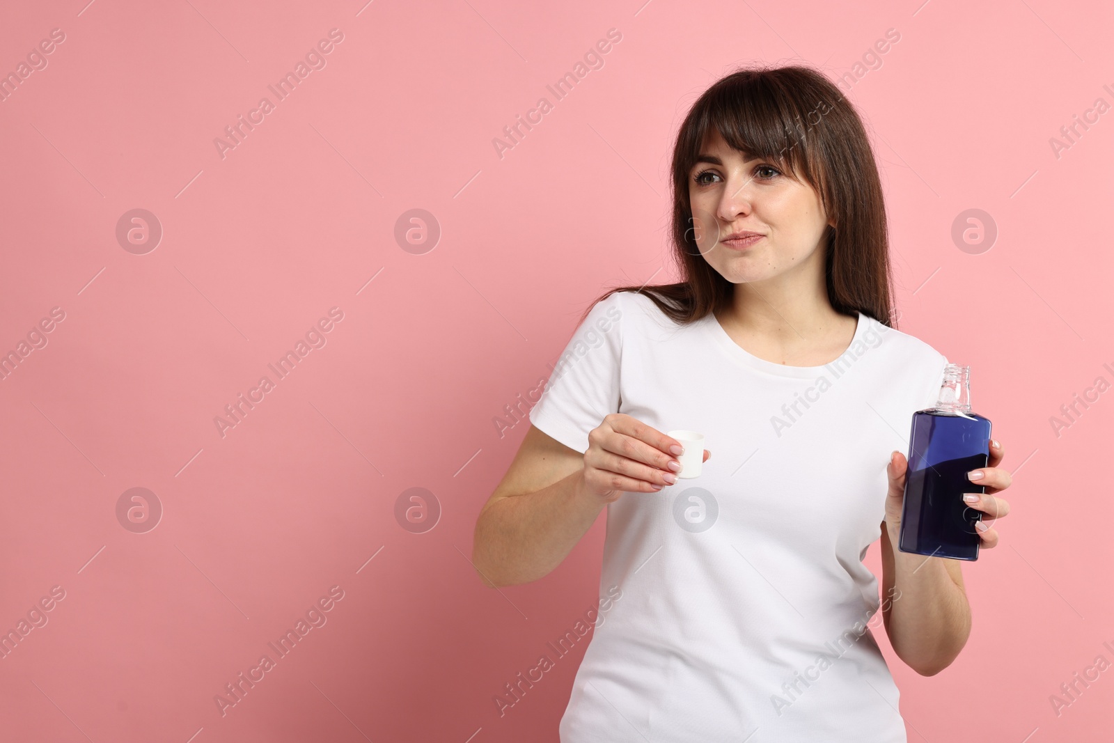 Photo of Young woman using mouthwash on pink background, space for text