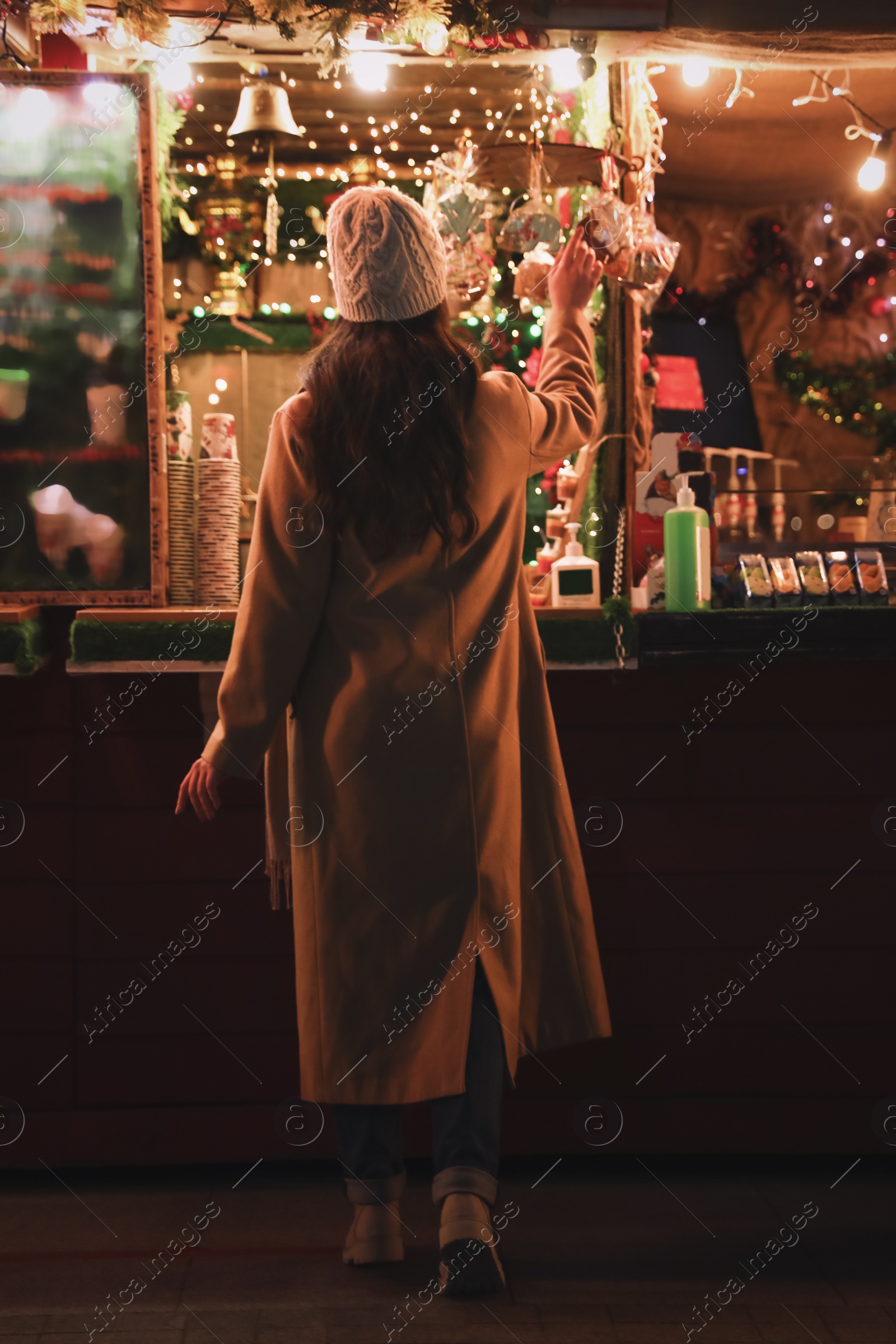 Photo of Young woman spending time at Christmas fair, back view