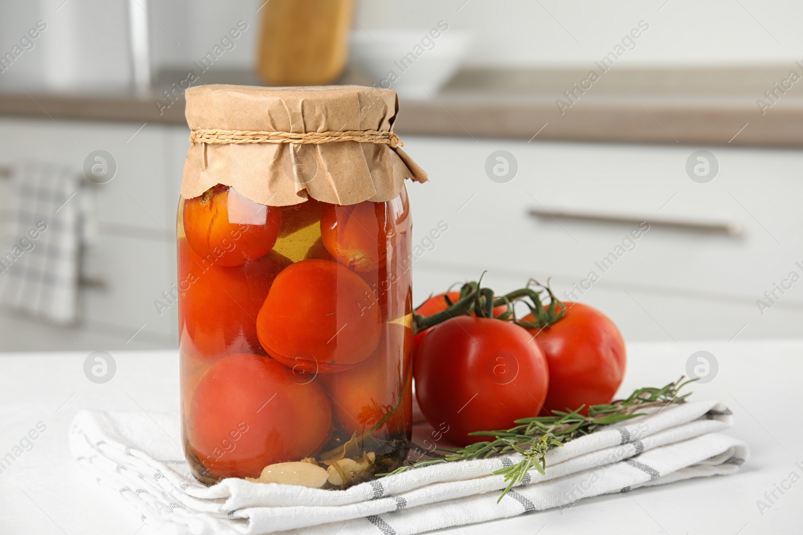 Photo of Pickled tomatoes in glass jar on white table in kitchen