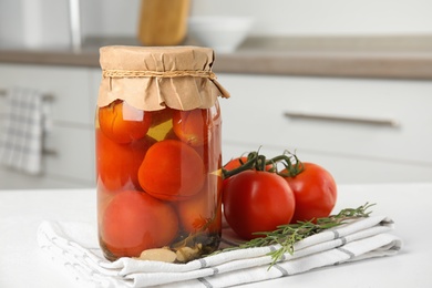 Photo of Pickled tomatoes in glass jar on white table in kitchen