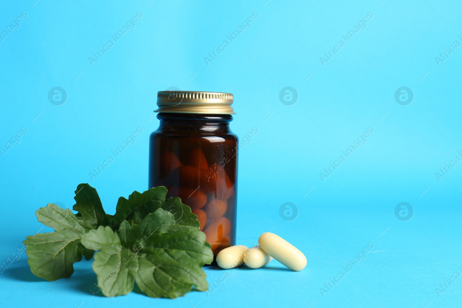 Photo of Medical bottle with pills and arugula on light blue background, space for text