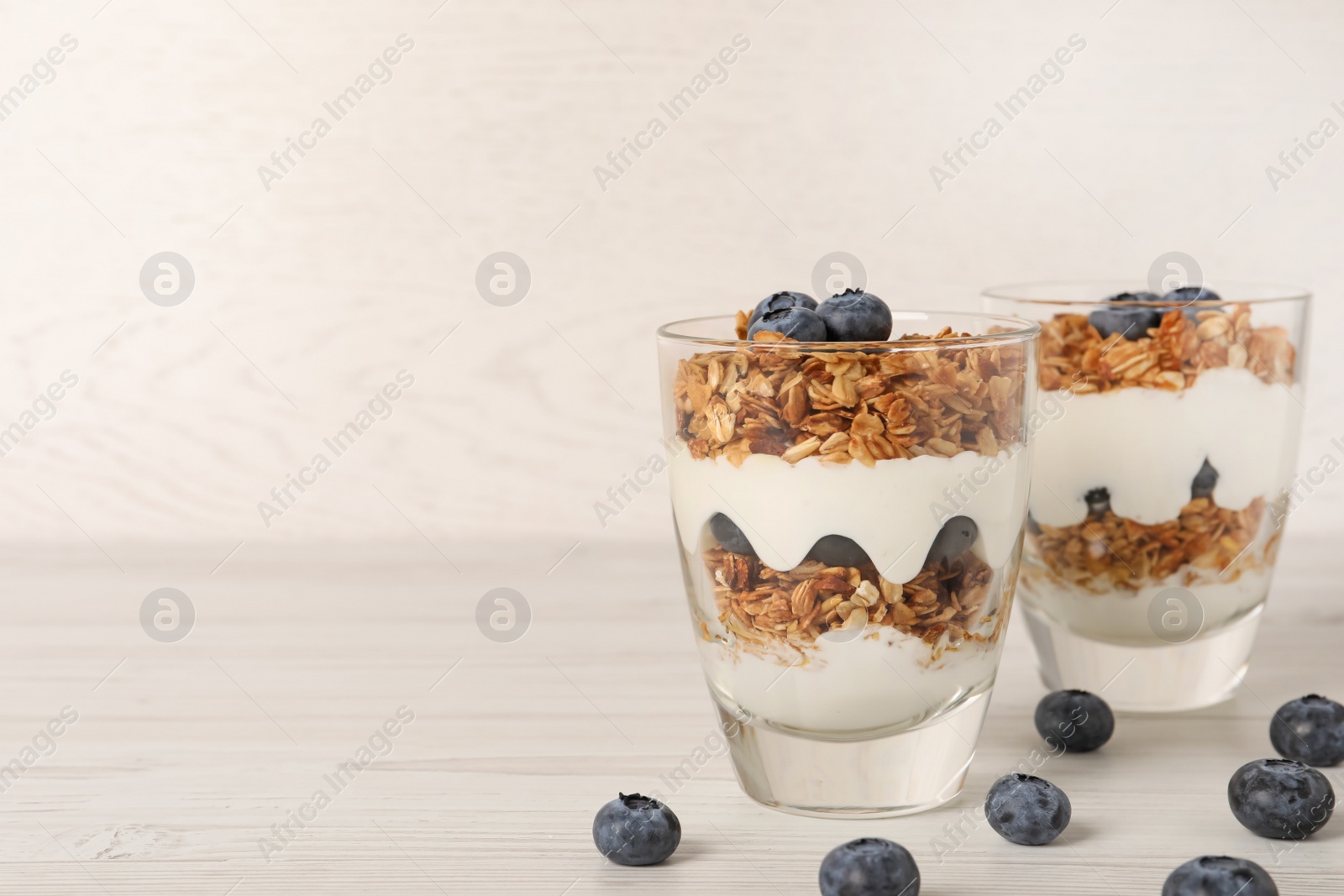 Photo of Glasses of tasty yogurt with muesli and blueberries served on white wooden table, space for text