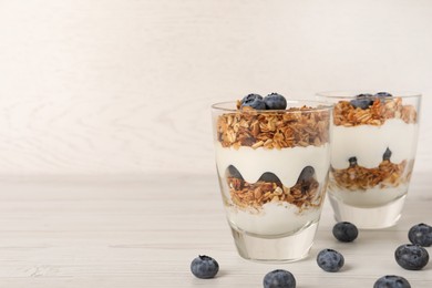 Glasses of tasty yogurt with muesli and blueberries served on white wooden table, space for text