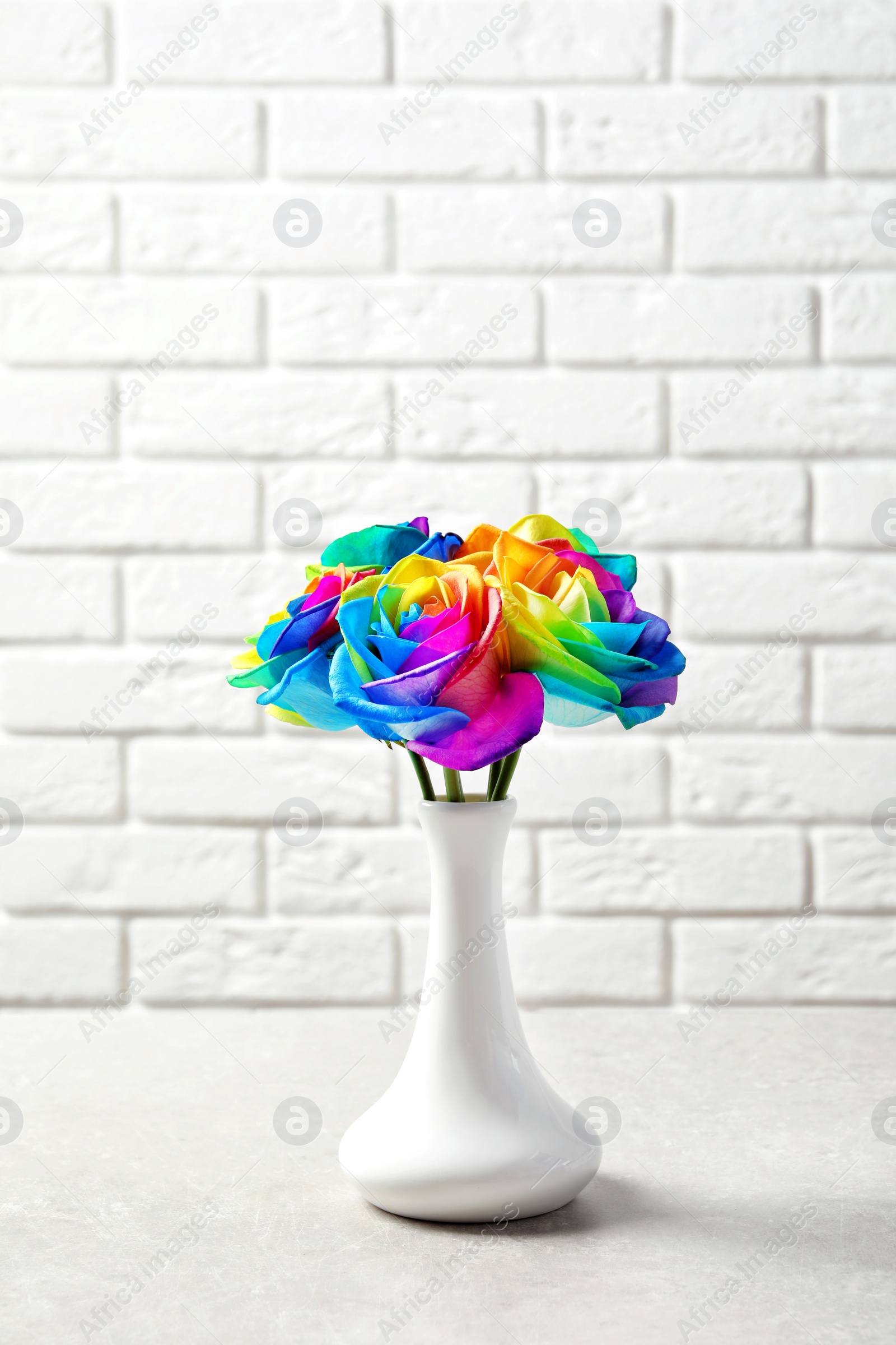 Photo of Vase with amazing rainbow rose flowers on table