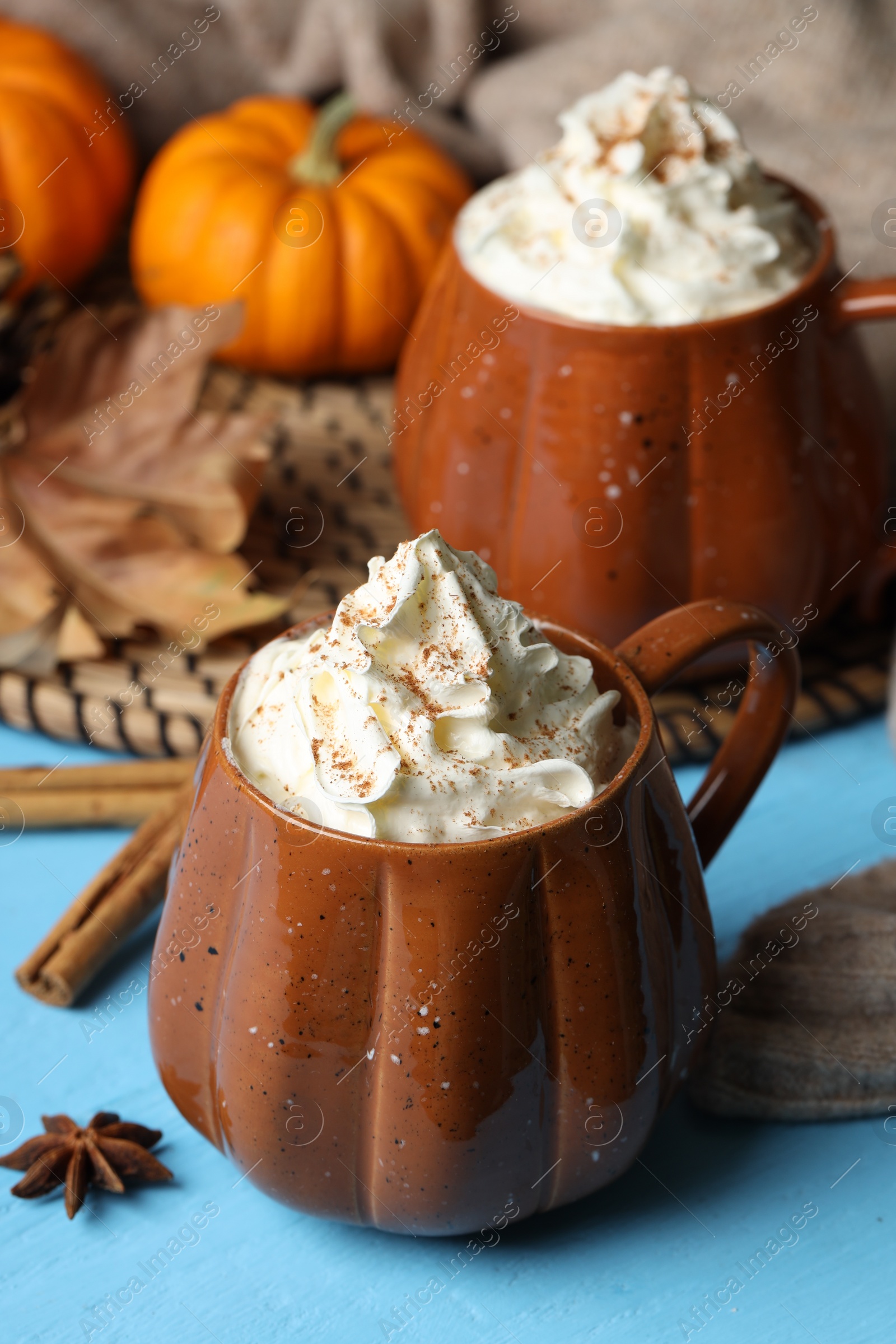 Photo of Mugs of pumpkin spice latte with whipped cream on light blue wooden table, closeup