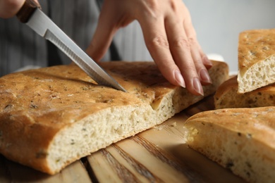 Photo of Woman cutting bread on wooden board, closeup