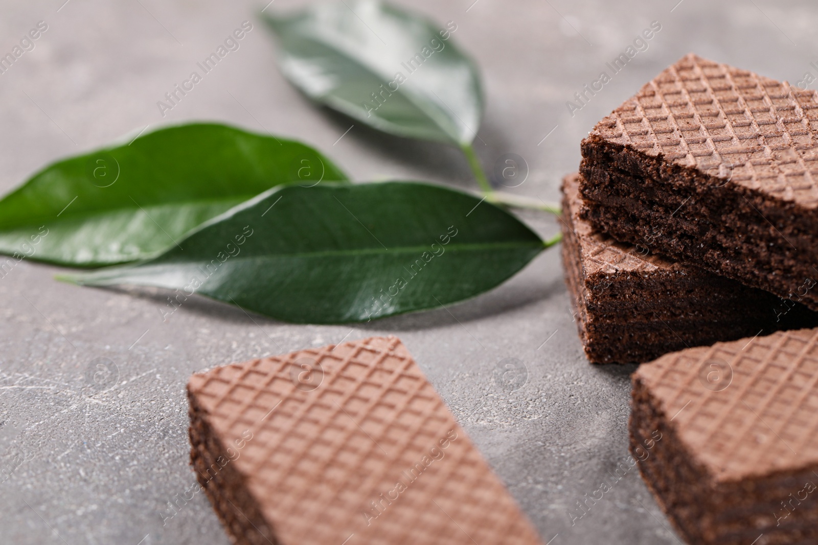 Photo of Delicious chocolate wafers with leaves on grey stone background, closeup. Space for text