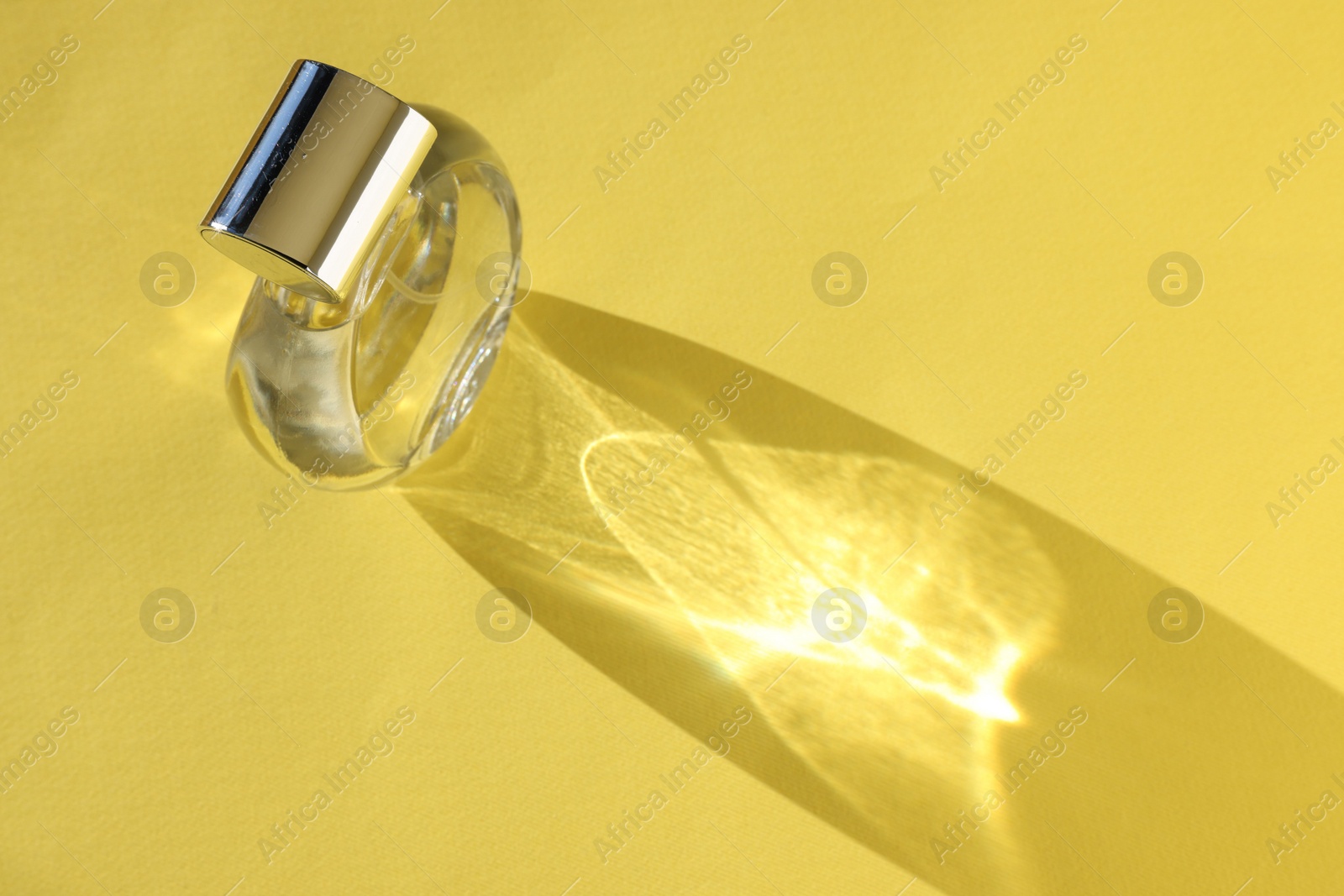 Photo of Luxury women's perfume. Sunlit glass bottle on yellow background, above view. Space for text