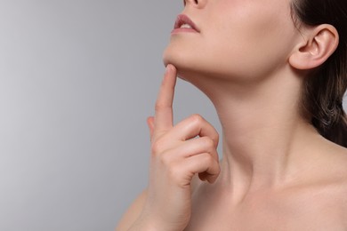 Young woman massaging her face on grey background, closeup. Space for text