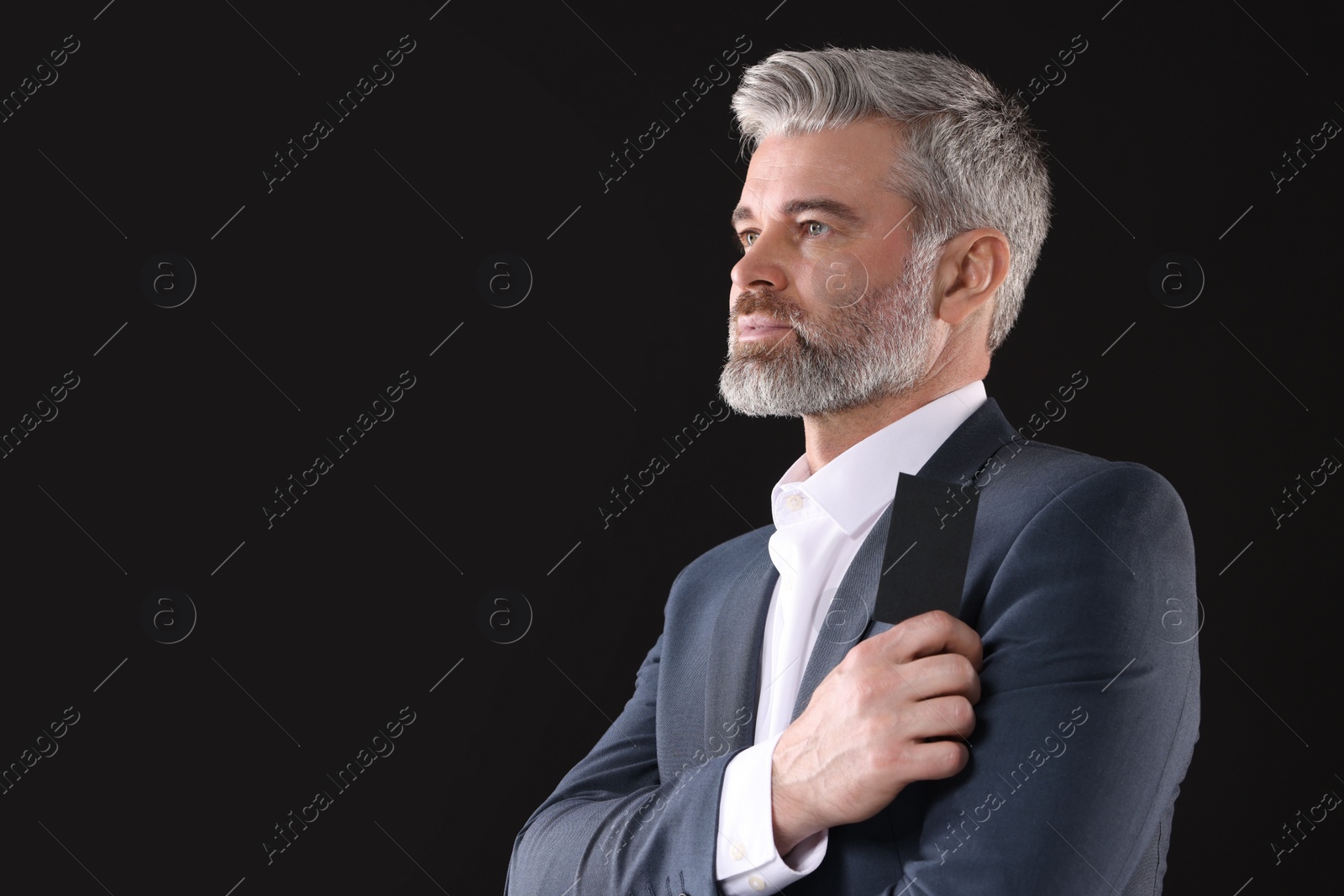 Photo of Handsome businessman holding blank business card on black background. Space for text