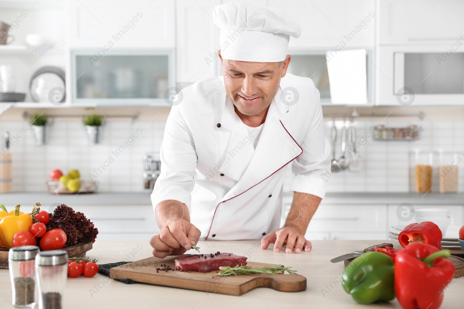 Photo of Professional chef cooking meat on table in kitchen